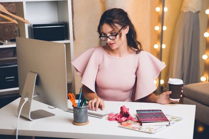fashion designer working at computer with coffee in studio
